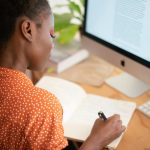 Woman in front of computer, writing in a notebook